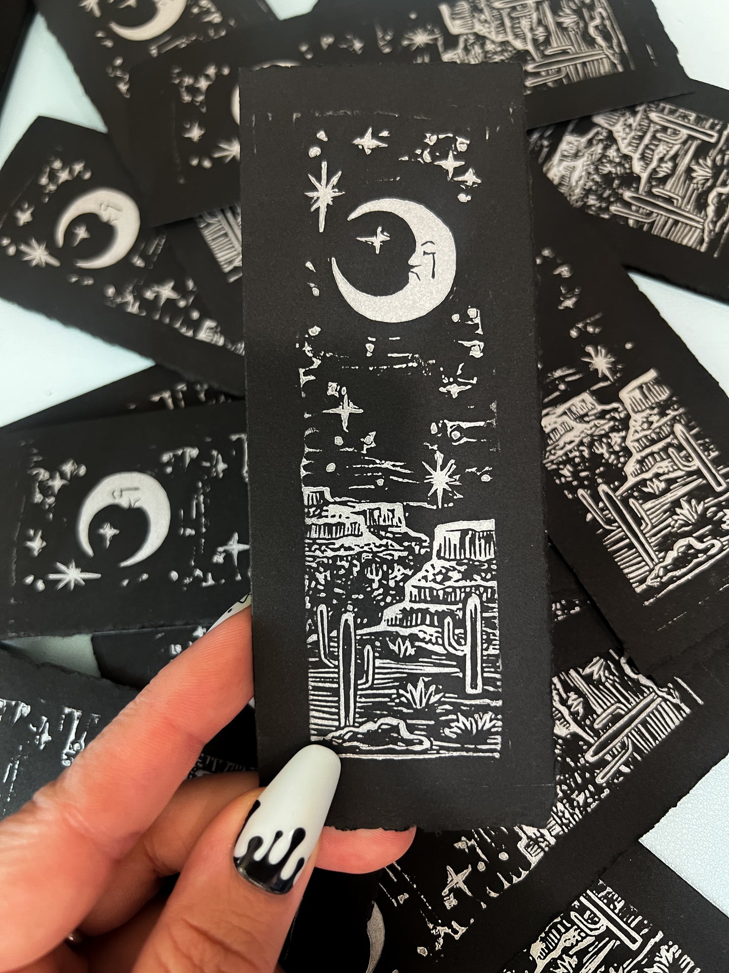 Handmade linocut bookmark of a sad crescent moon face on archival paper