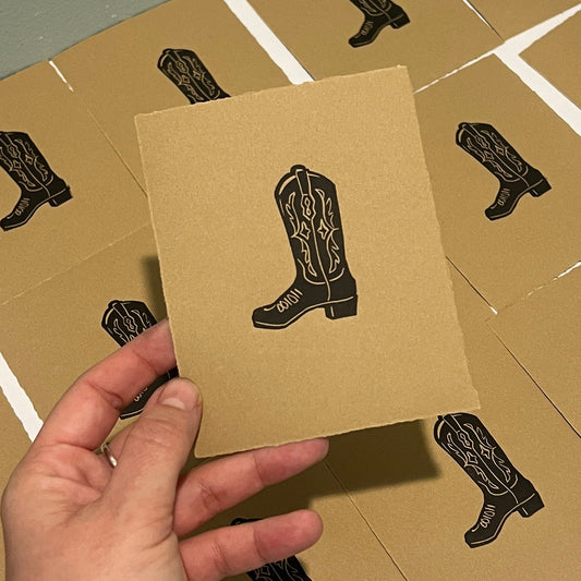 Handmade mini linocut print of a boot in black ink on kraft brown paper