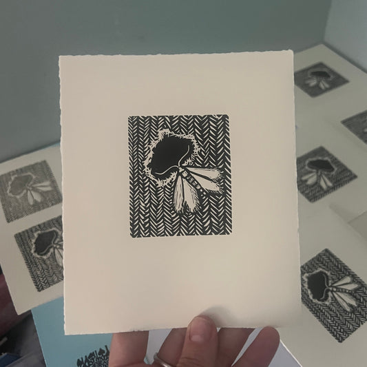 Handmade mini linocut print of a clothes moth eating knit fabric in black ink on warm white paper