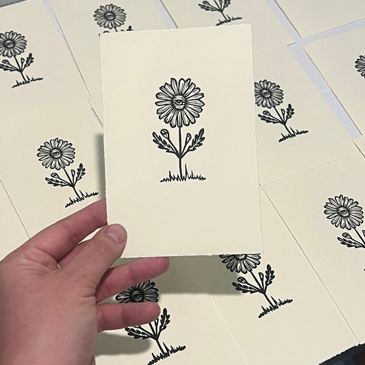 Handmade mini linocut print of a floral eye design in black ink on warm white paper