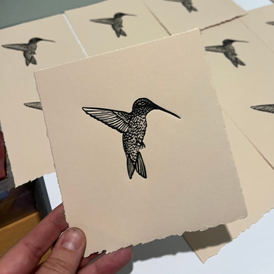 Handmade mini linocut print of a hummingbird in black ink on fawn tan paper