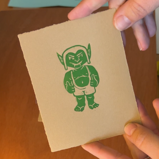 Handmade mini linocut print of a green goblin giving two thumbs up in green ink on kraft brown paper