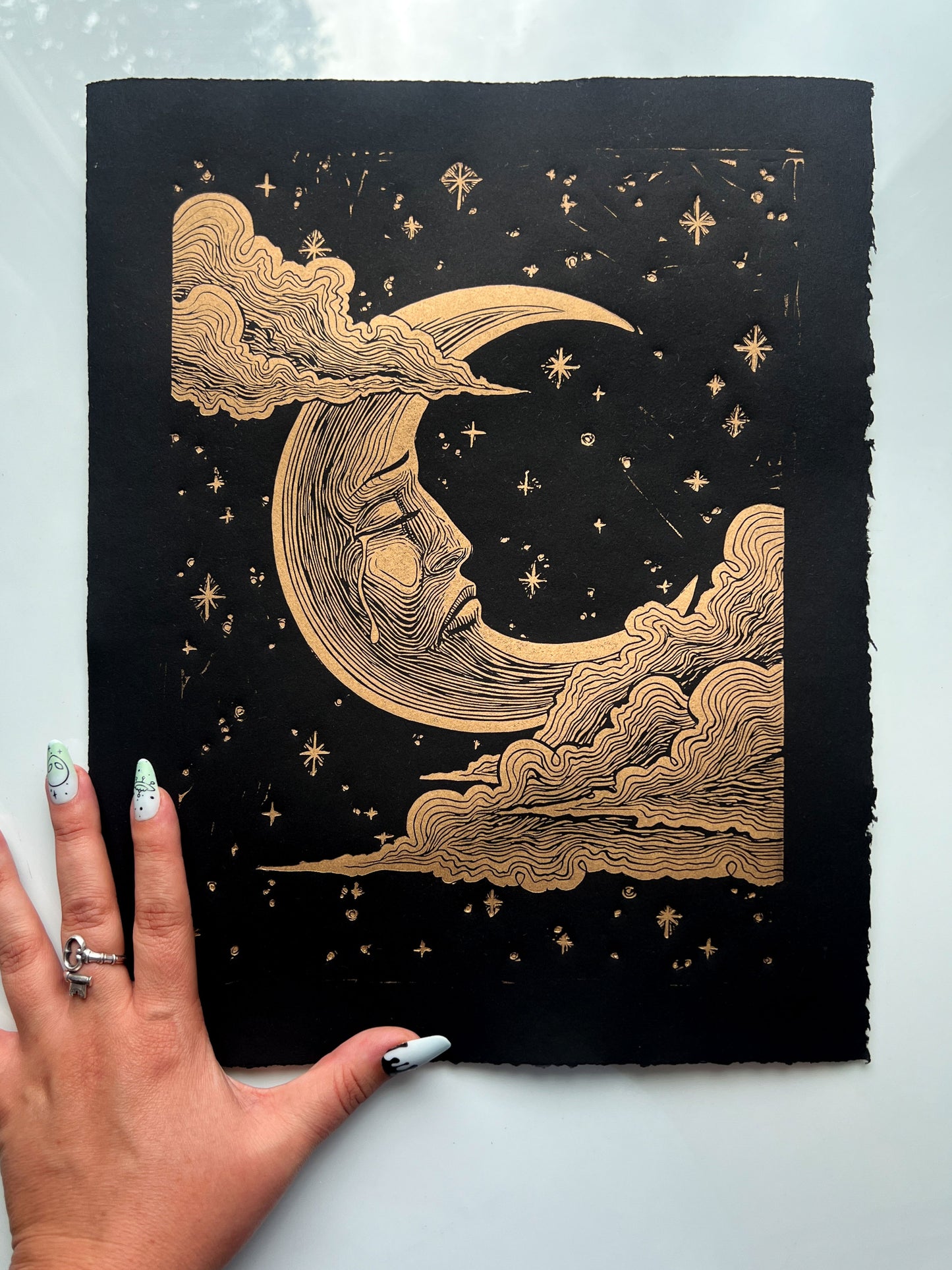 Handmade linocut print of a sad crescent moon face on archival paper