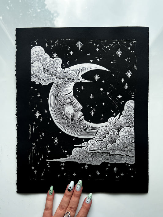 Handmade linocut print of a sad crescent moon face on archival paper