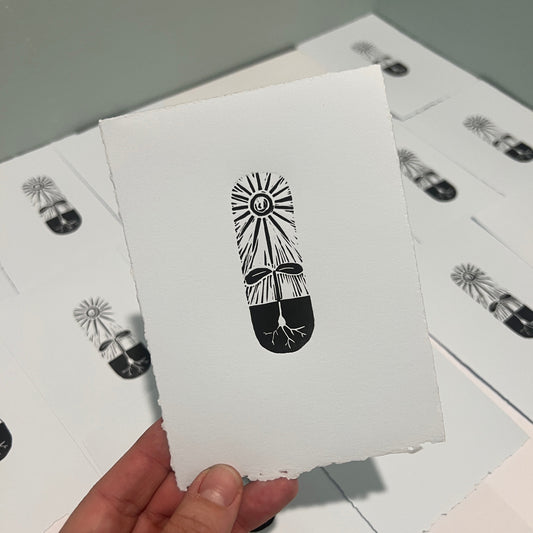 Handmade mini linocut print of a sun in black ink on pale blue paper, tall narrow format